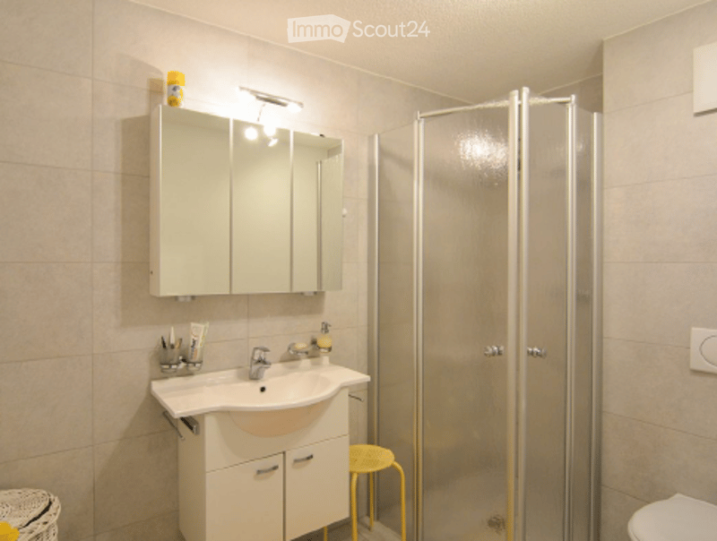 Modern bathroom with a white sink, mirror cabinet, glass shower stall, and a small yellow stool.