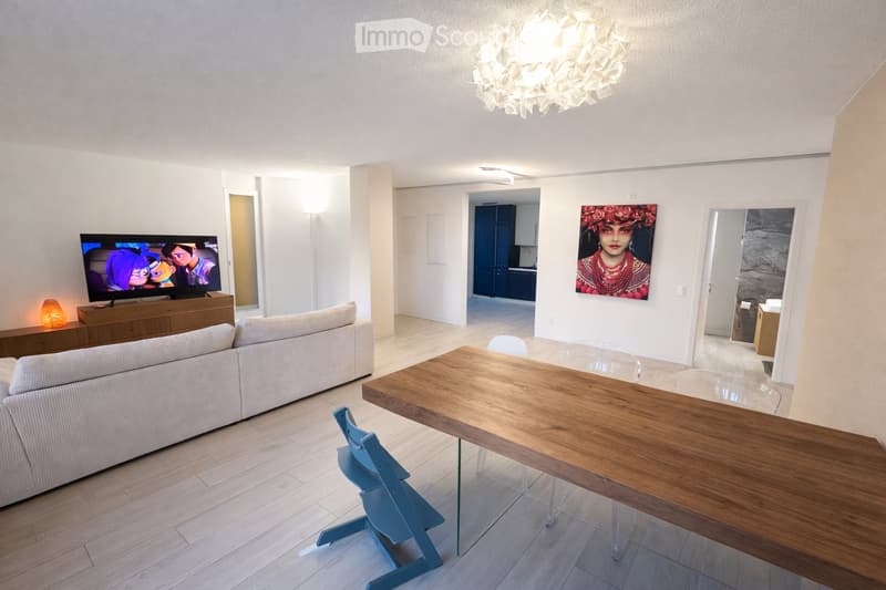 Modern living room with a white sofa, wooden coffee table, dining table with chairs, TV, and artwork on the wall.