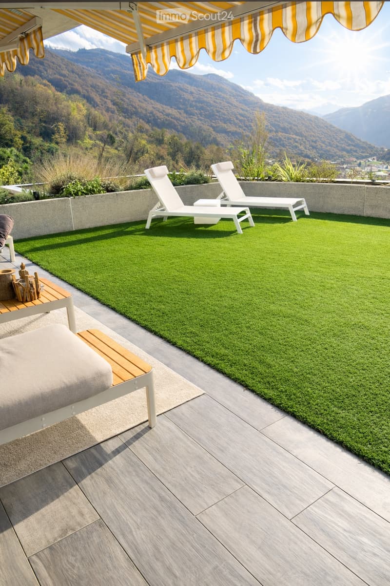 Deck with artificial grass and wooden loungers under awning, surrounded by mountains
