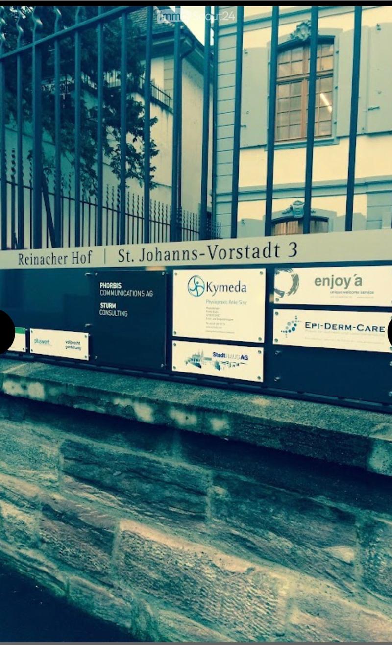 Exterior view of a building with a metal fence and company logos on the wall, including "Reinacher Hof | St. Johanns-Vorstadt 3" signage.