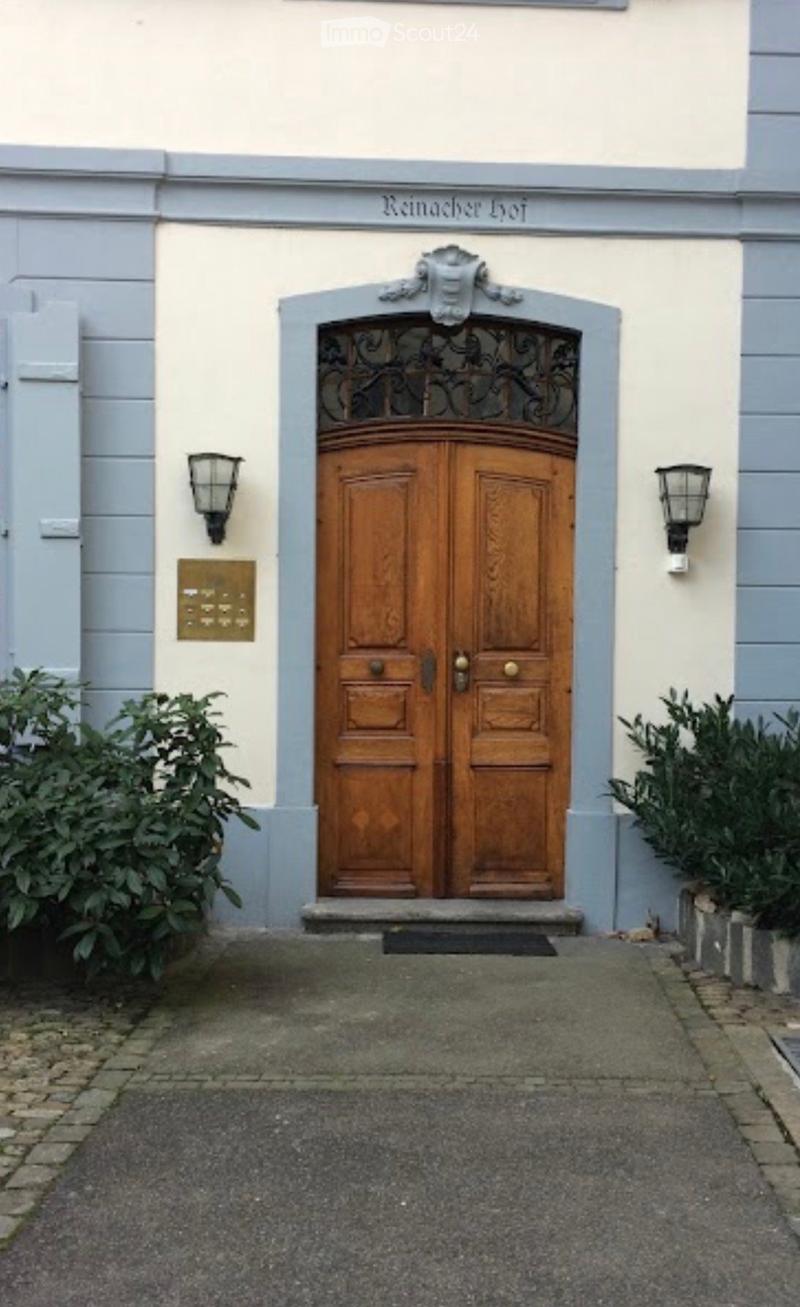 Entrance to a building with a double wooden door, ornate metalwork above, and decorative wall-mounted lanterns on either side.