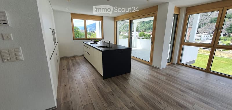 Modern kitchen with wooden flooring, large windows offering a scenic view, and a central island with a sink and faucet.