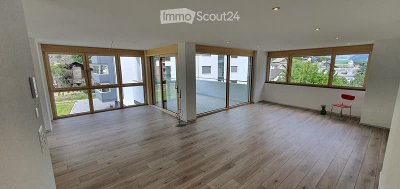 Bright, unfurnished room with large windows and wooden flooring, featuring a single red chair and a small plant near the window.
