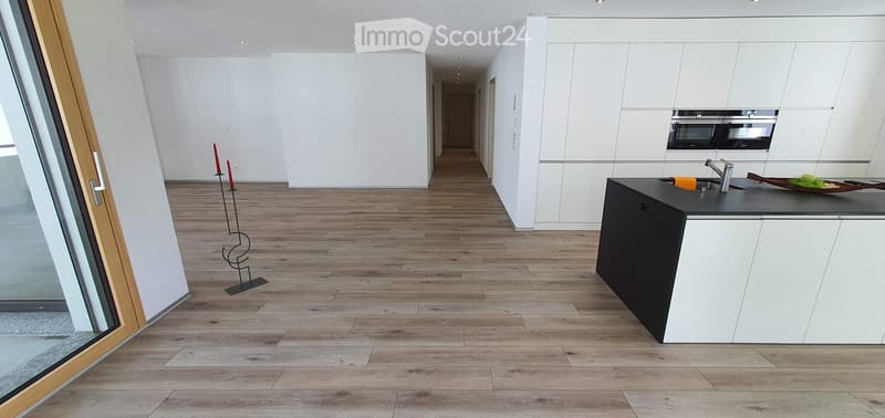 Modern kitchen with white cabinets, black island, and wooden flooring. Features a sleek faucet, built-in oven, and decorative candle holders.