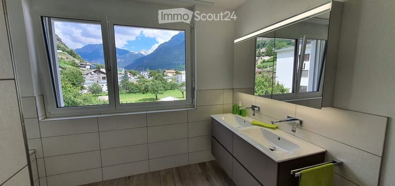 Modern bathroom with double sink, large mirror, and scenic mountain view through large windows.