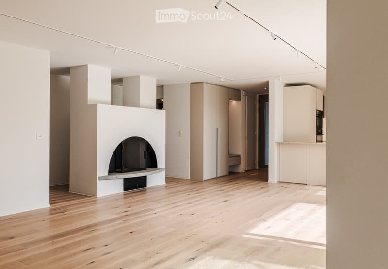 Open, minimalist room with light wooden flooring, white walls, and a built-in fireplace. The space is empty, with no furniture or furnishings visible.