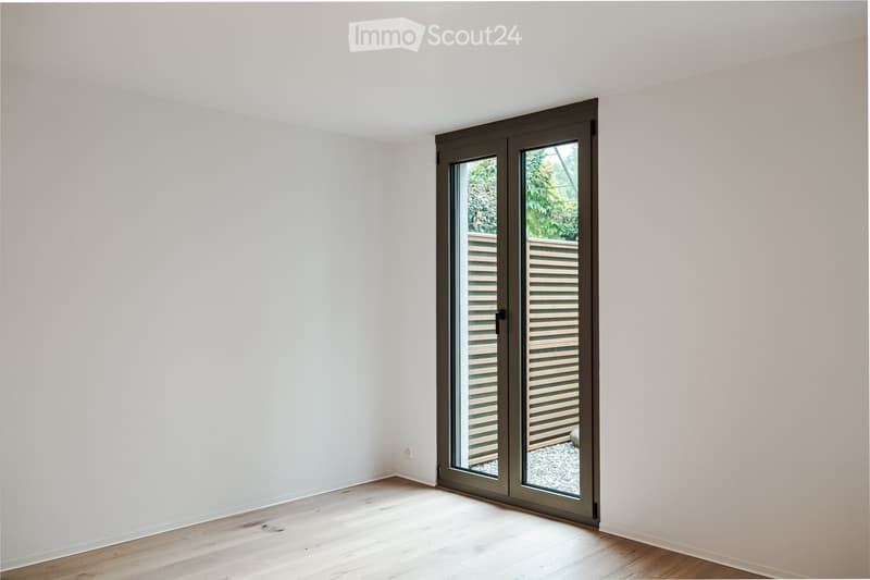 Empty room with light-colored walls and wooden flooring, featuring a large sliding glass door leading to an outdoor area.