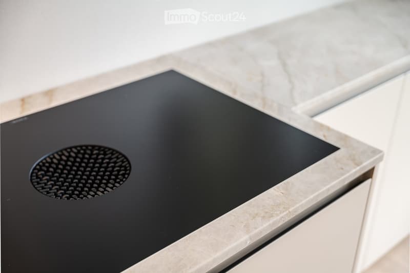 Close-up of a sleek black induction cooktop with a circular burner, integrated into a modern kitchen with marble countertops and white cabinetry.