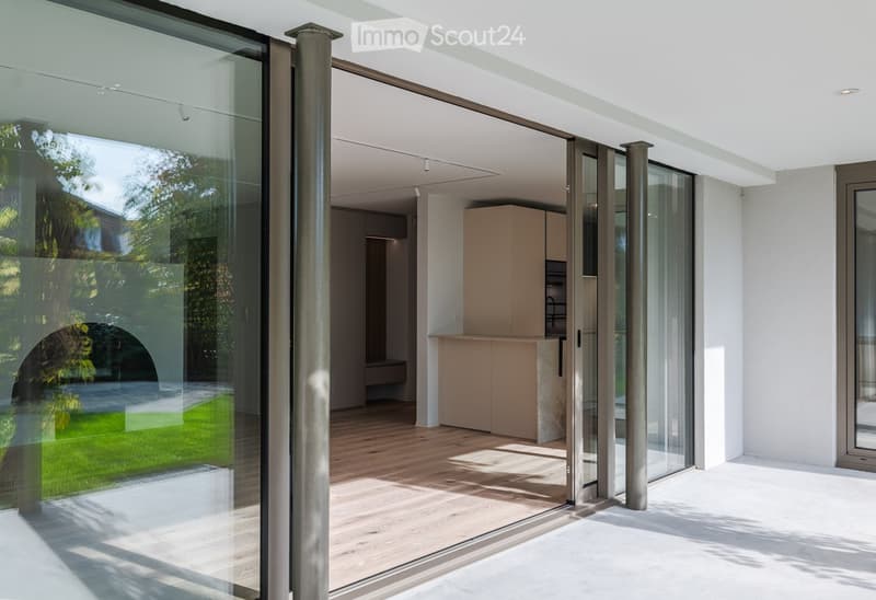 Modern kitchen with light-colored cabinets, a countertop, and large glass sliding doors leading to a patio area with wooden flooring.