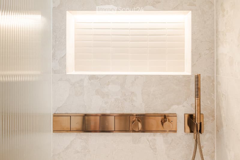 Modern bathroom shower area with a sleek, gold-colored control panel and a large, square showerhead mounted on marble walls.