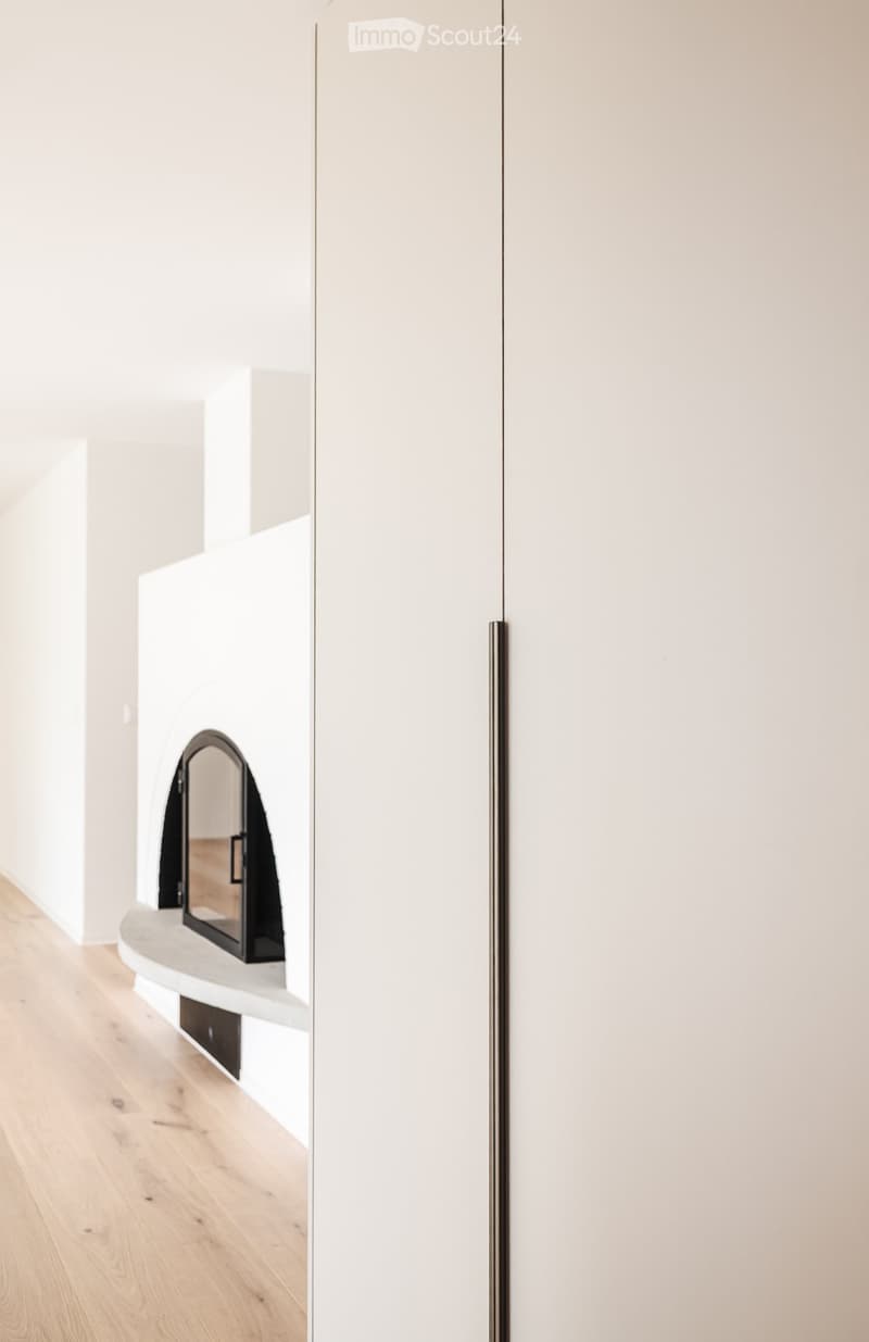 A modern hallway with light-colored walls, a sleek white cabinet, and a small built-in shelf with a mirror. The floor is light wood.