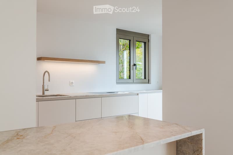 Modern kitchen with white cabinets, marble countertop, stainless steel sink, and a sleek faucet. A window with a view of greenery is visible above the sink.