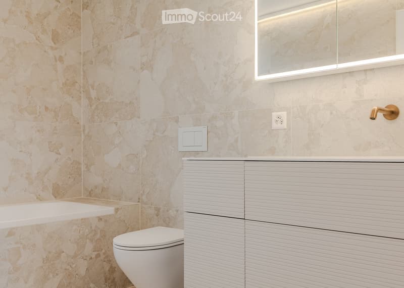 Modern bathroom with marble tiled walls, a white toilet, a sleek sink cabinet, and a large mirror with integrated lighting.