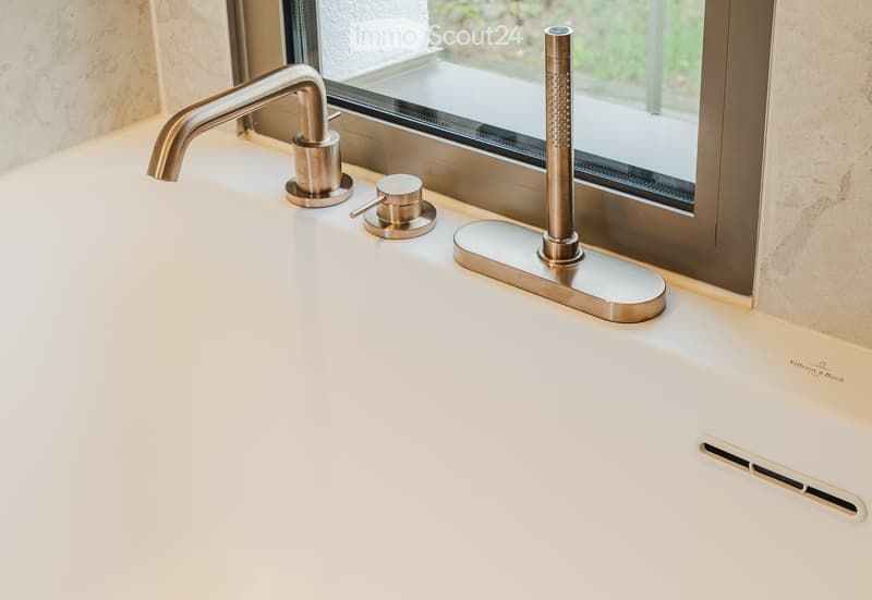 Modern bathroom sink with a sleek, chrome faucet and controls, placed near a large window with a view of greenery.