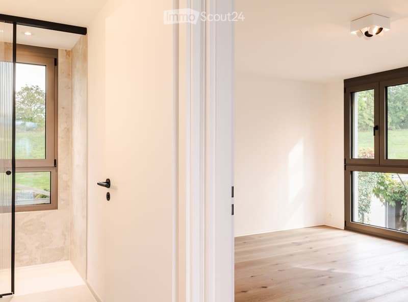 Empty hallway with light-colored walls, wooden flooring, and large windows on both sides, allowing natural light to fill the space.