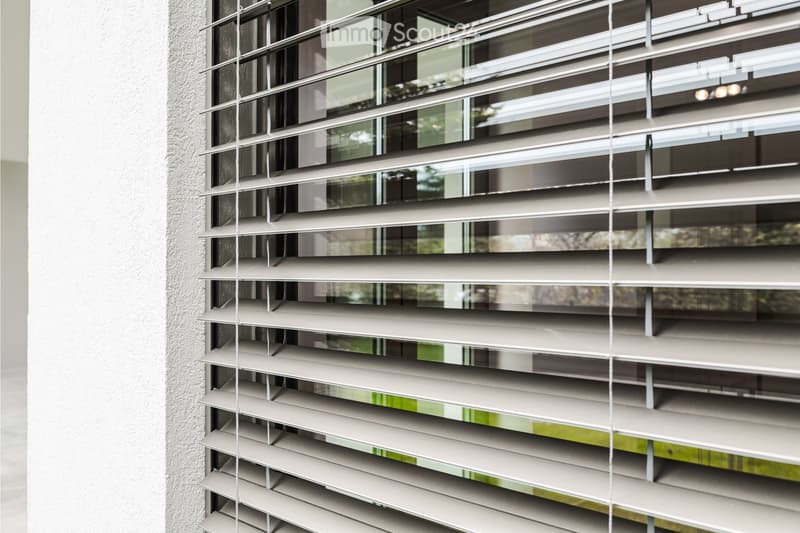 Close-up of modern roller blinds on a window, with a textured wall visible to the left.