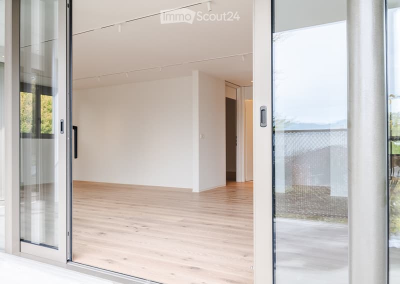 Empty room with light wooden flooring, white walls, and large glass sliding doors leading to an outdoor area.