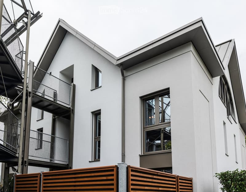 Modern two-story house with white exterior, large windows, and a metal balcony on the upper level.
