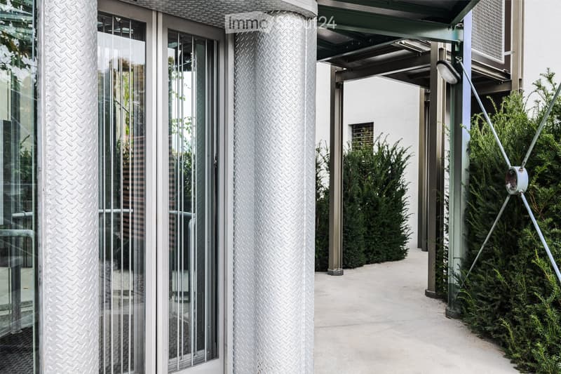 Modern outdoor area with glass doors, textured columns, and neatly trimmed evergreen shrubs.