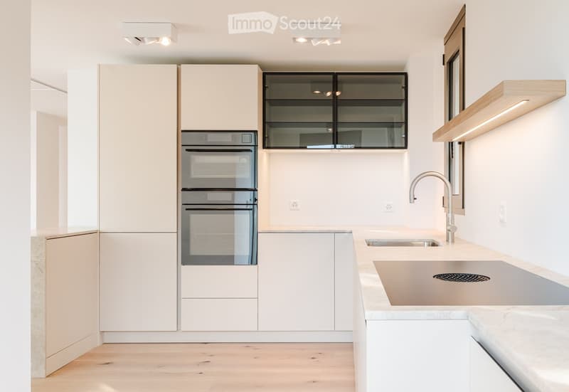 Modern kitchen with light-colored cabinets, a double sink, a sleek faucet, and a built-in oven. The space features wooden flooring and recessed lighting.