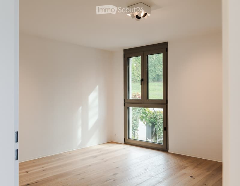 Empty room with light-colored wooden flooring, white walls, and a large sliding glass door leading to a garden area.