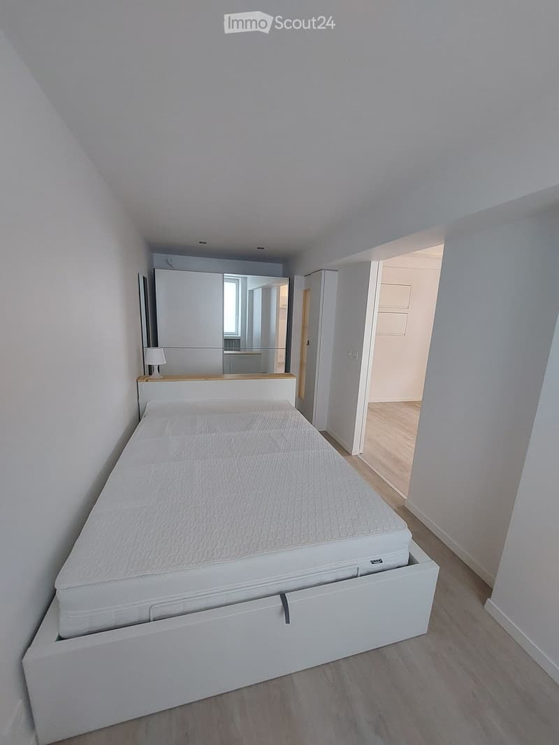 Modern bedroom with a white bed, built-in storage, a mirror, and a small lamp on the nightstand.