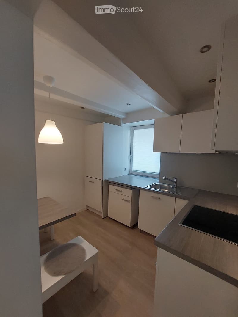 Modern kitchen with white cabinets, wooden floor, sink, faucet, and a small table with a stool.