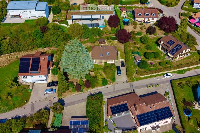 Aerial view of a residential neighborhood with multiple houses, solar panels on rooftops, and surrounding greenery.