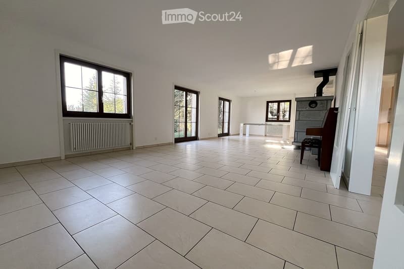 Empty room with tiled floor, large windows, radiators, and a small table near the wall.