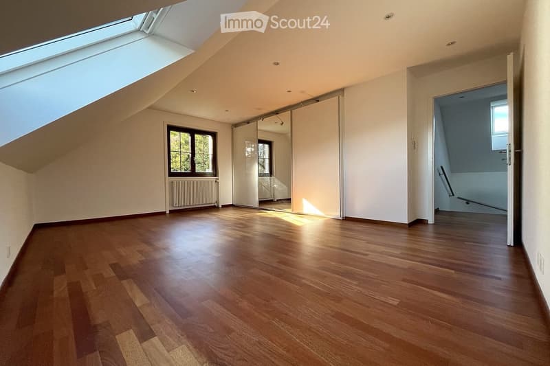 Empty room with wooden flooring, white walls, large skylight, and a window with a radiator below it. A sliding door leads to another room, and a staircase is visible in the background.