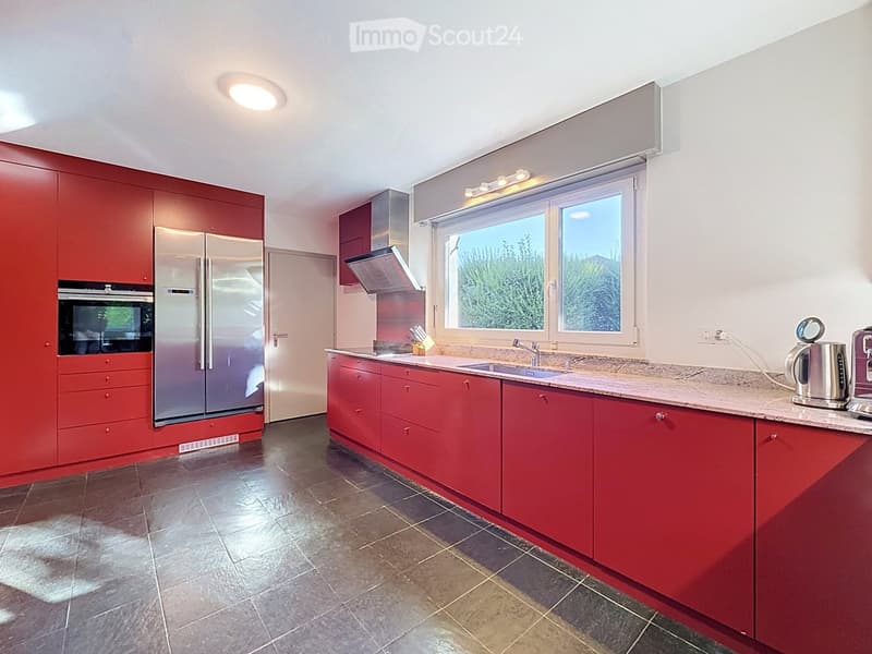 Modern kitchen with red cabinets, stainless steel appliances, granite countertop, and large windows.