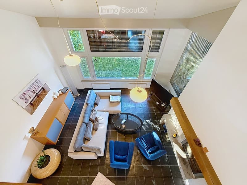 Modern living room with a sectional sofa, coffee table, two blue armchairs, pendant lights, a TV, and a small plant on a round table.