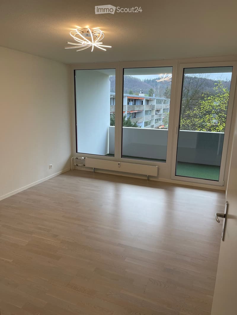 Empty room with wooden flooring, large windows, and a modern ceiling light fixture.
