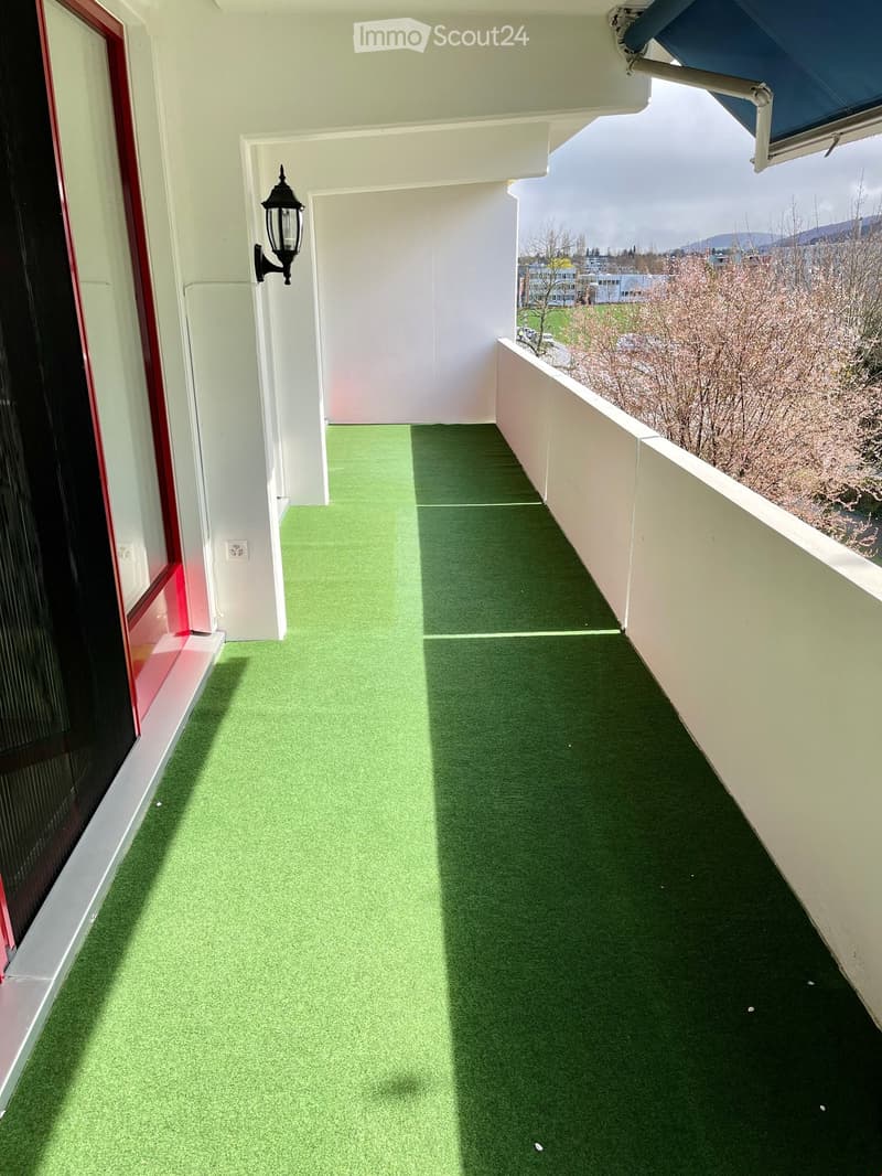 Balcony with green artificial turf flooring, white walls, and a view of the surrounding area.