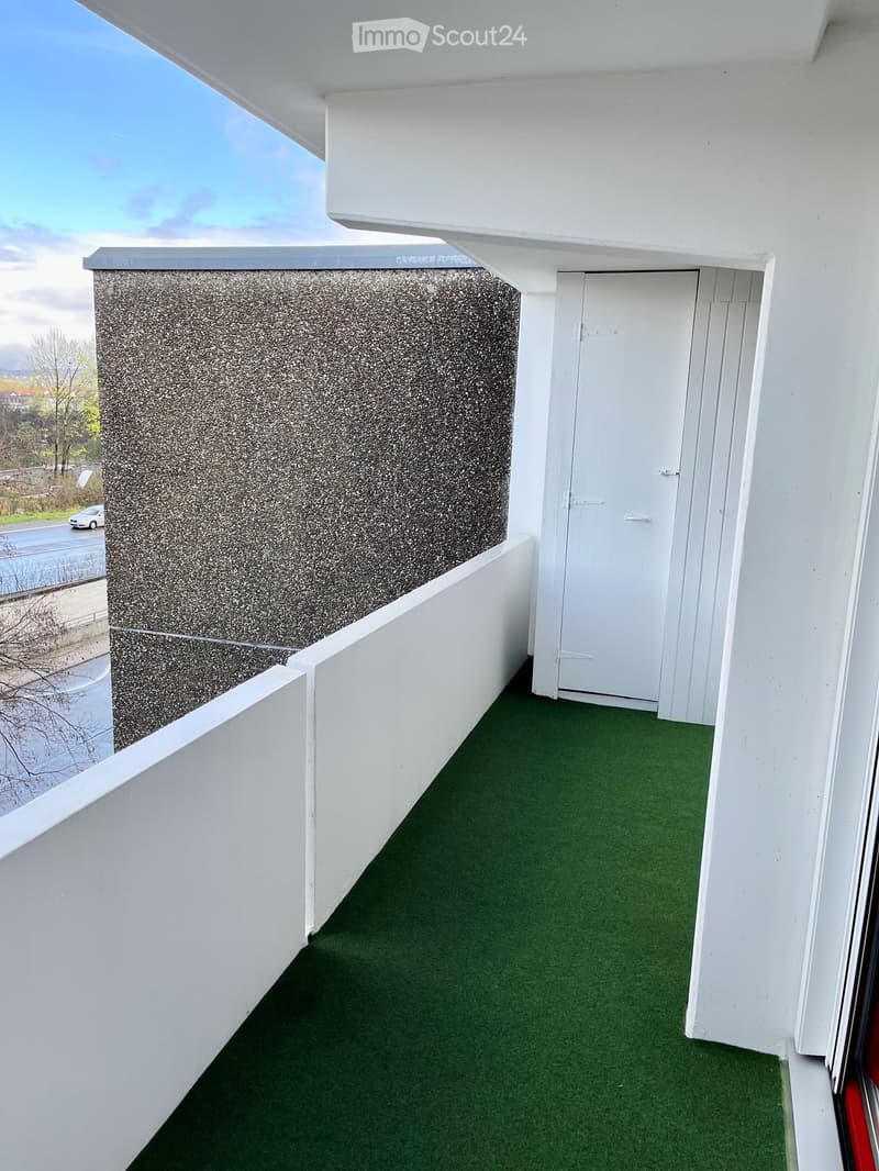 Balcony with green artificial turf flooring, white walls, and a door leading inside.