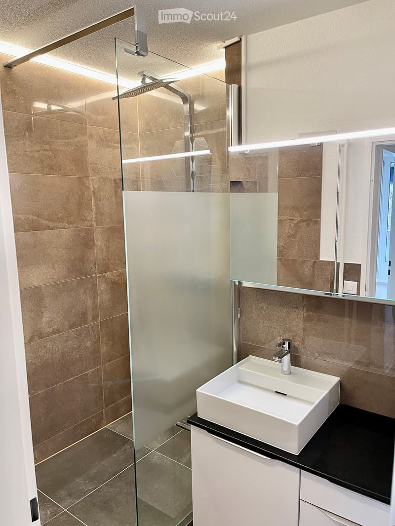 Modern bathroom with a white sink, chrome faucet, glass shower enclosure, and beige tiled walls.