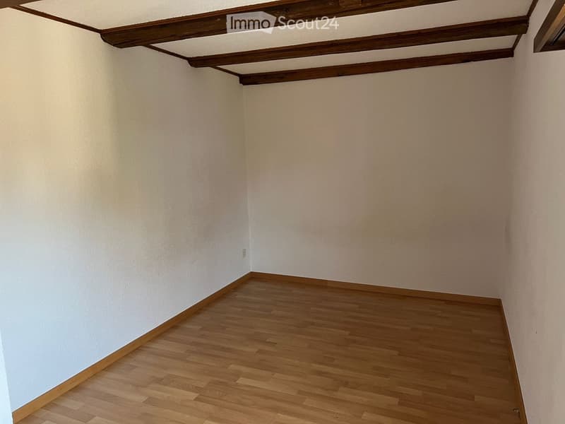 Empty room with wooden flooring and white walls, featuring exposed wooden beams on the ceiling.