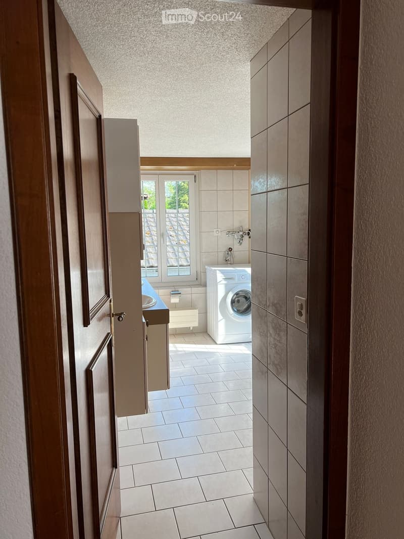 Modern bathroom with white tiled floor, white washing machine, sink, and window offering outdoor view.