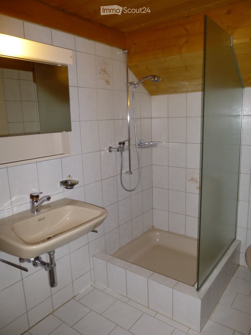 Bathroom with a sink, mirror, bathtub, and glass shower enclosure. The walls and floor are tiled, and the ceiling has wooden paneling.