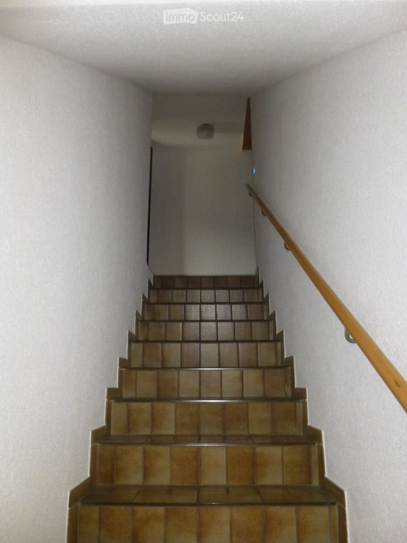Staircase with beige tiled steps and a wooden handrail, leading upwards.