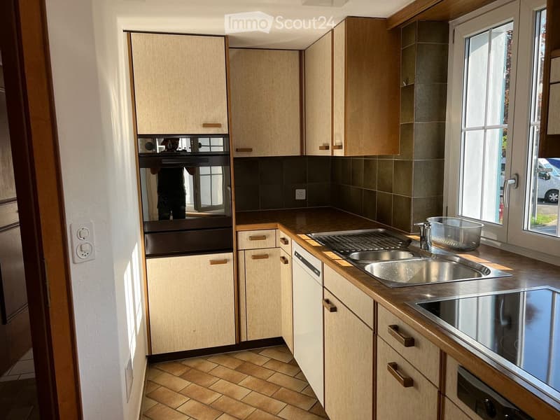 Modern kitchen with light wooden cabinets, stainless steel appliances, and a tiled floor.