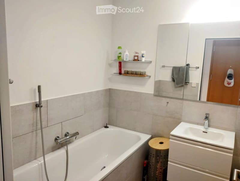 Modern bathroom with a bathtub, sink, mirror, and shelves holding toiletries and decorative items.