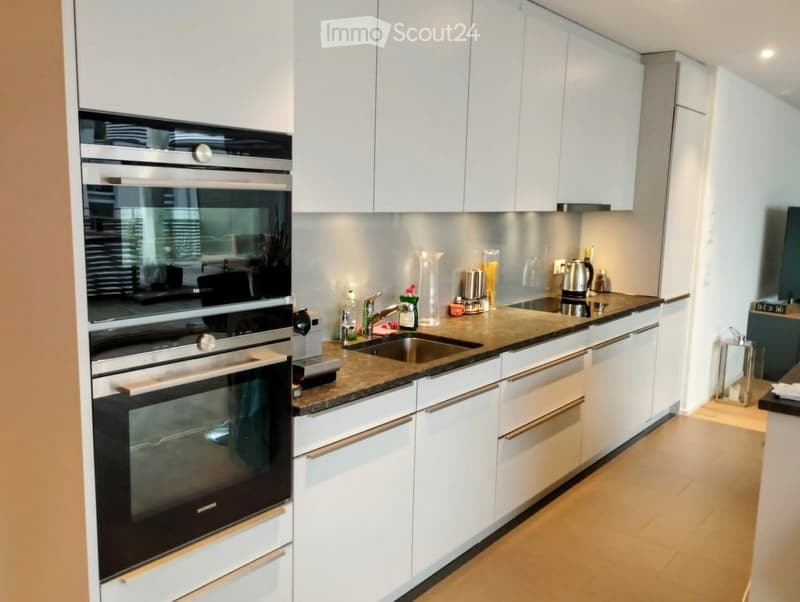 Modern kitchen with white cabinets, stainless steel appliances, granite countertop, and various kitchen items including a coffee maker and a candle.