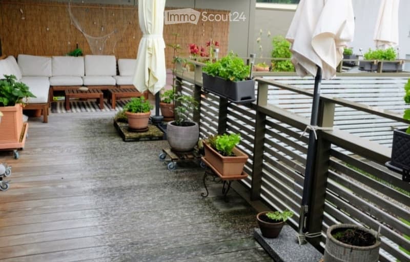 Balcony with wooden decking, white sofa seating area, potted plants, and outdoor umbrella.
