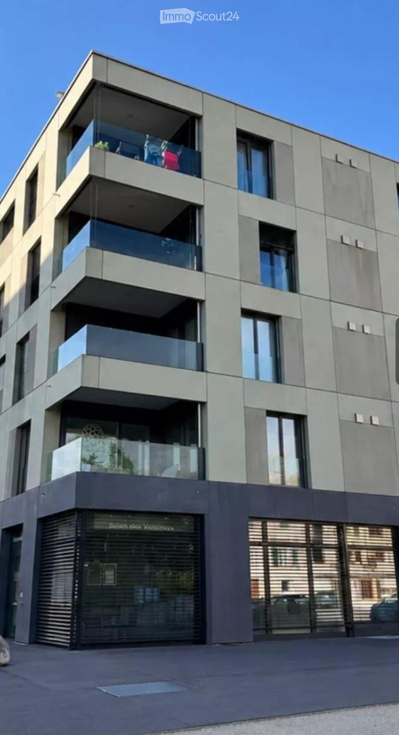 Modern multi-story building with balconies and large windows, featuring a contemporary design with grey and white facade.
