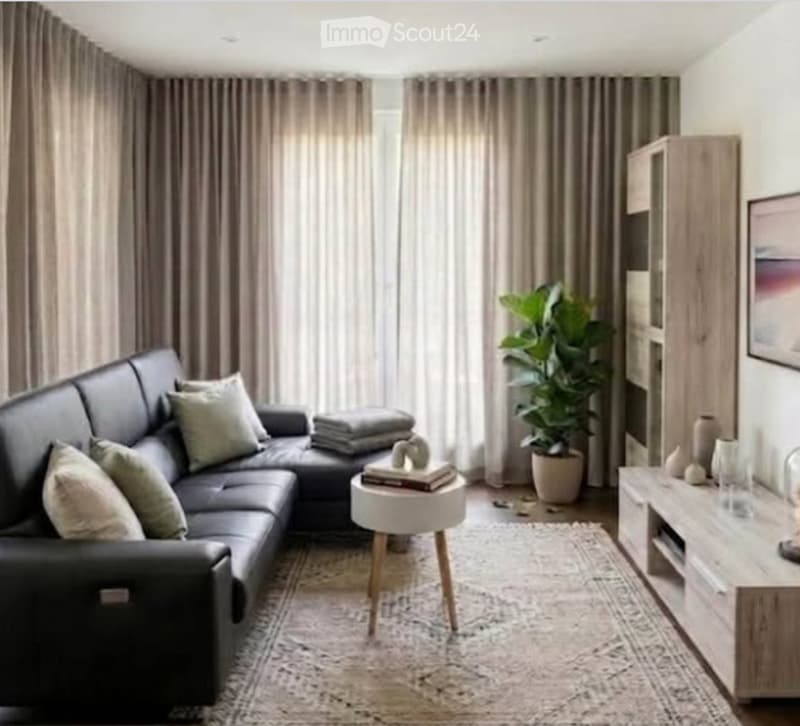 Modern living room with a black leather sectional sofa, a white coffee table, a side table, a potted plant, a wooden cabinet, and a picture frame on the wall.