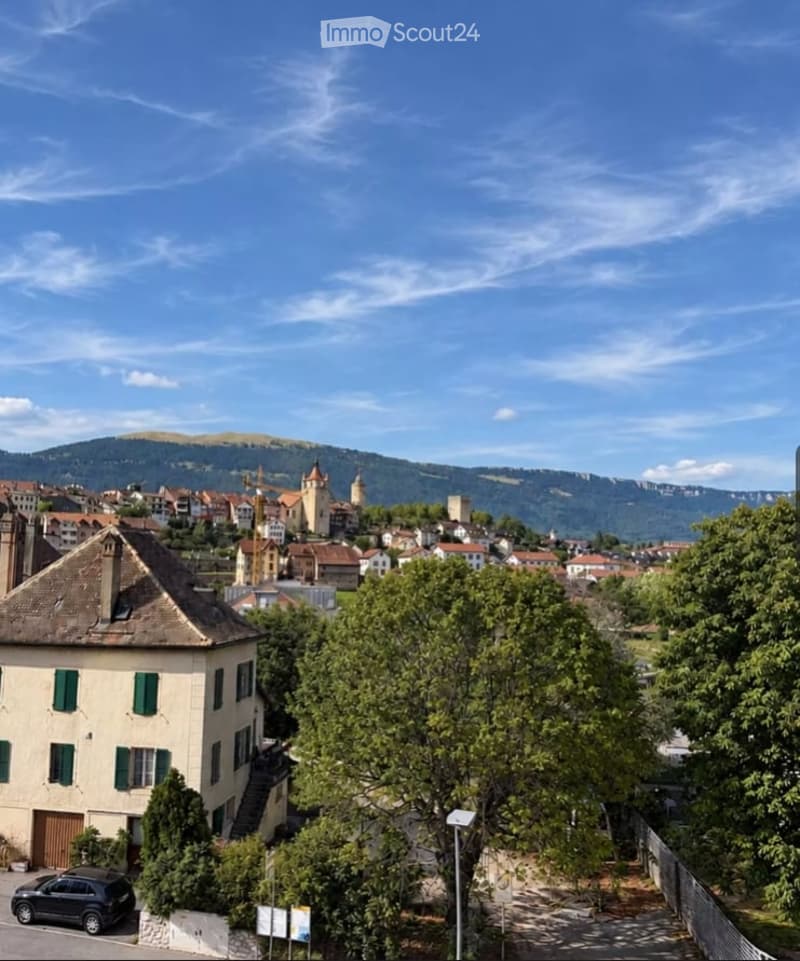 View of a town with traditional houses, green trees, and distant mountains under a clear blue sky.
