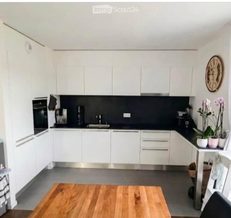 Modern kitchen with white cabinets, stainless steel appliances, and a wooden dining table.