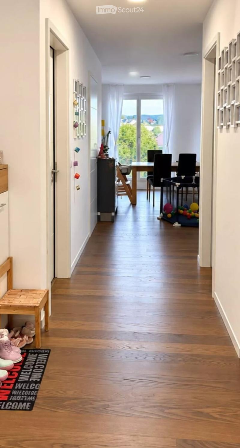 Bright hallway with wooden flooring, leading to a dining area with a table and chairs, and a view of a garden through large windows.