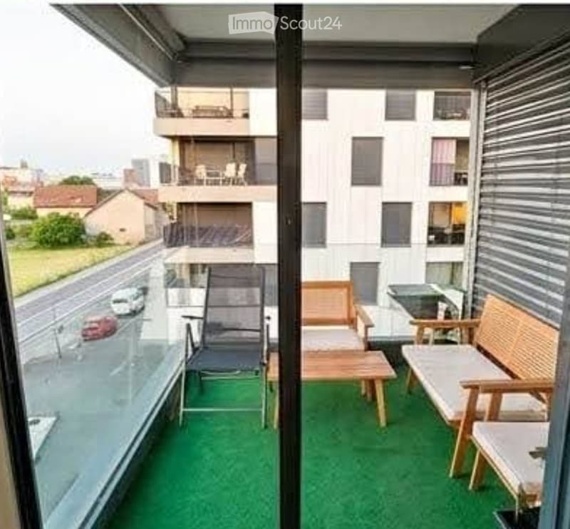 Balcony with green artificial turf, wooden bench, chairs, and small table.